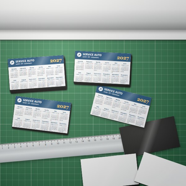 Calendare magnetice personalizate de 90 × 50 mm în teancuri, pe planșa de tăiere, lângă rola de folie magnetică și o riglă metalică
